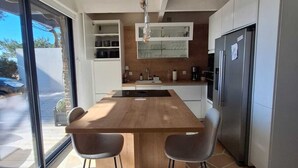Una cocina moderna con una isla central, dos taburetes de bar, un refrigerador y un ventanal grande.