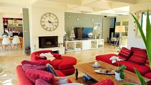 Una sala de estar amplia con sofás rojos, una chimenea, un reloj grande y un televisor.