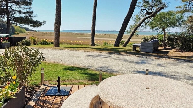 Un patio con una mesa redonda y bancos, con vistas a una playa y una perspectiva despejada del mar y la costa distante.
