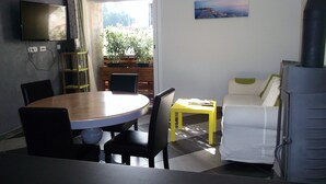Un espace de vie compact comprenant une table à manger, des chaises, un canapé, un téléviseur fixé au mur et un tableau.
