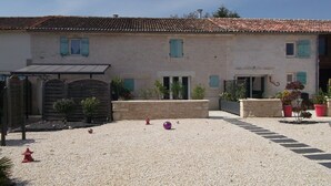 Une cour avec un sol en gravier, un bâtiment doté d’un toit en tuiles et un portail.