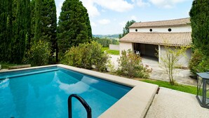 Une piscine à l’eau d’un bleu limpide, entourée de verdure et bordée d’un bâtiment dont le toit est recouvert de tuiles.
