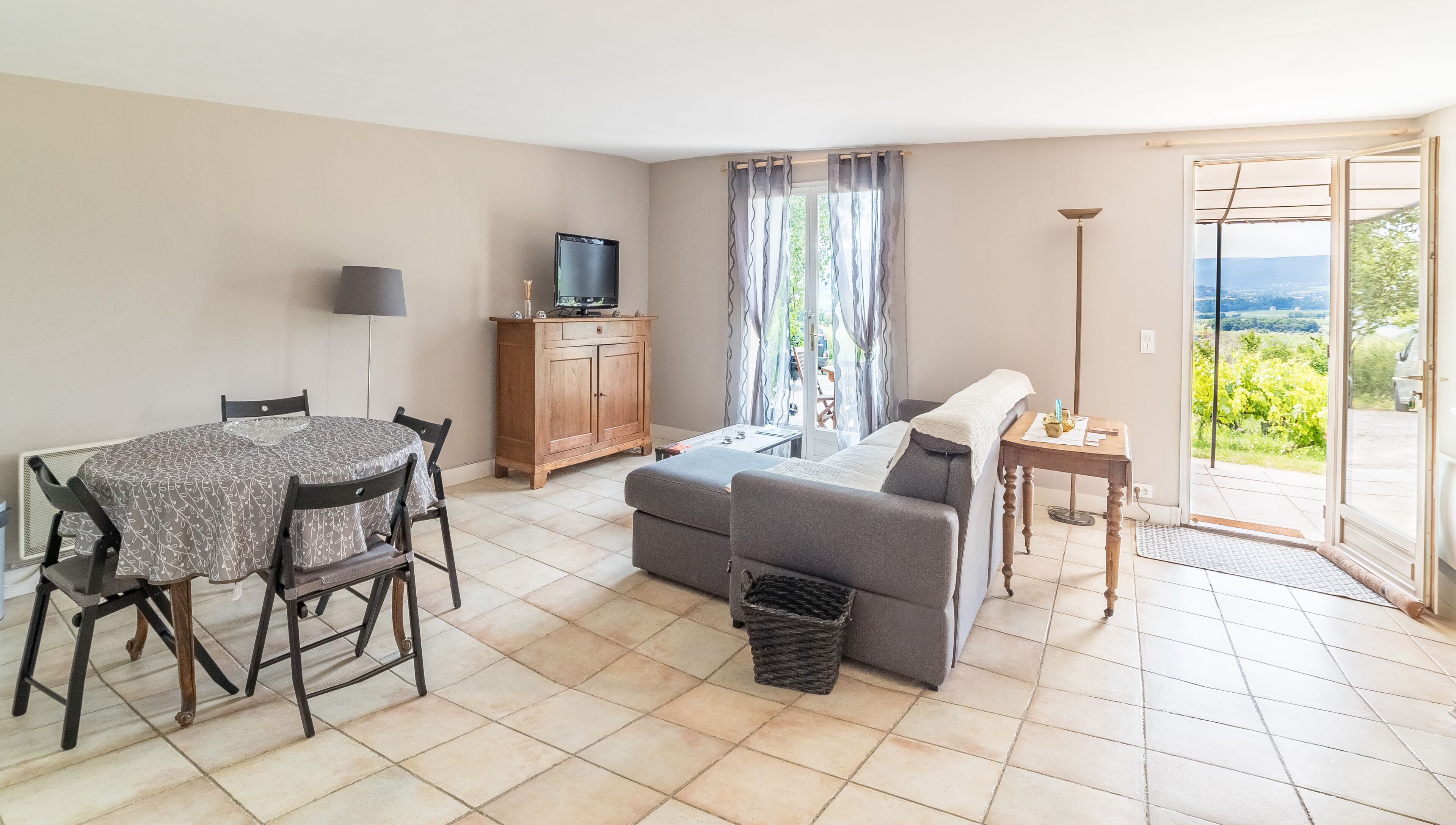 Una sala de estar con sofá, una mesa de comedor con sillas, un televisor y vistas al exterior.
