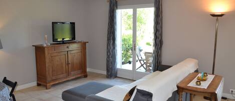 Una habitación con sofá gris, armario de madera, televisor y una mesa con lámpara.