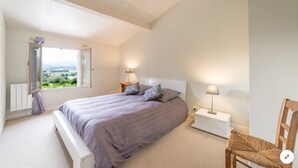 Une chambre à coucher avec un lit, des tables de chevet, une chaise et une vue sur l’extérieur, grâce à une porte ouverte.