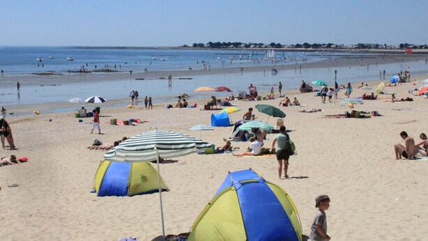 Uma praia com tendas, guarda-sóis e pessoas.