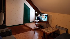 Um quarto pequeno e acolhedor, com teto inclinado, televisão, mesa de madeira e uma cadeira.