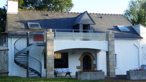 Uma casa de dois andares com escada em espiral, varanda coberta e arco de pedra.