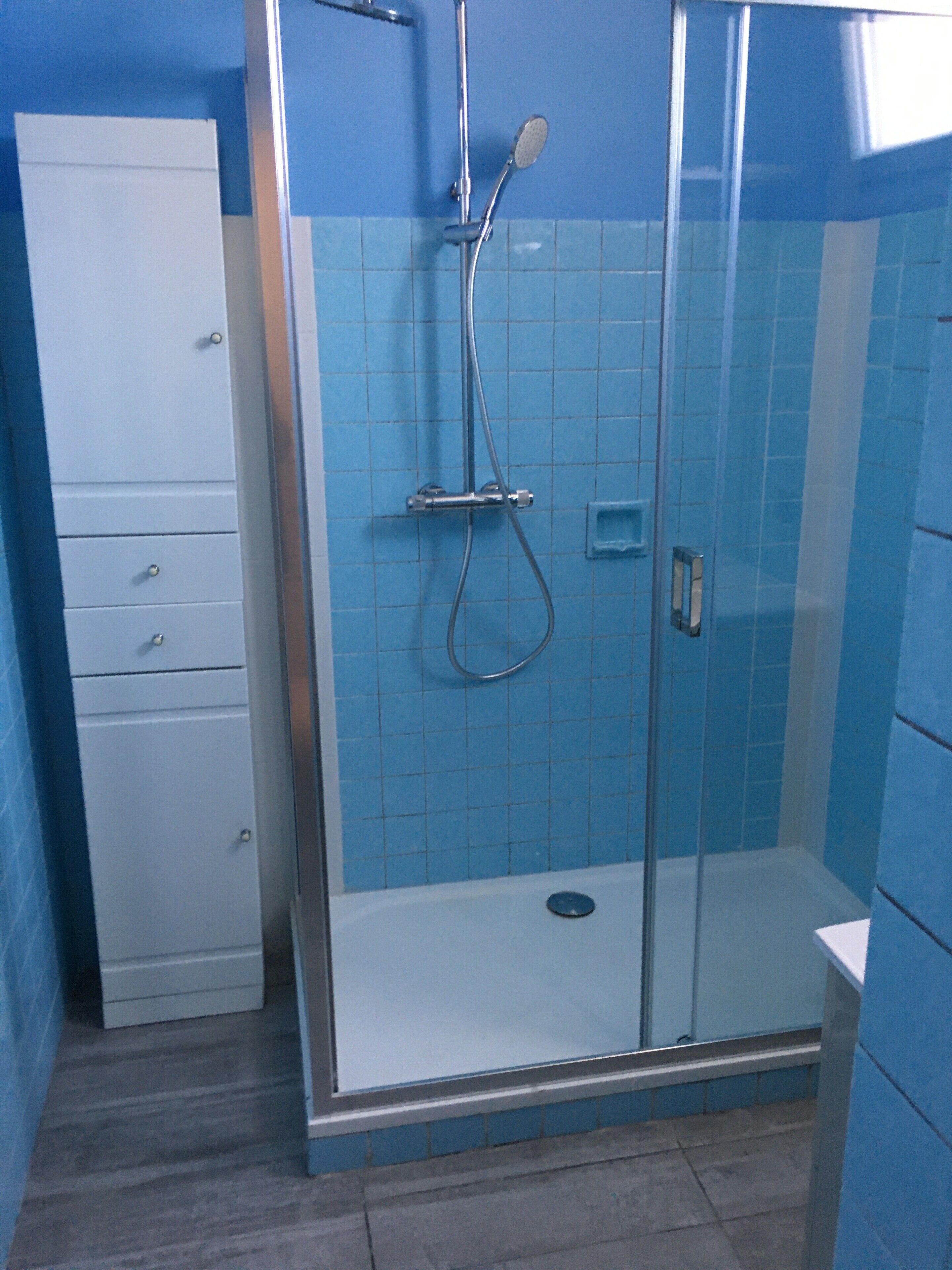 Ducha con cerramiento de vidrio, cabezal de ducha de mano y llave de pared.
