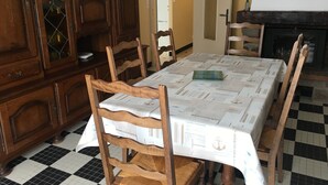 A dining area with a checkered floor, wooden chairs, a table covered with a patterned tablecloth, a wooden cabinet with glass doors, and a wall clock. - INDEPENDENT HOUSE CLOSE TO SEA AND PORT LA GRAVETTE 50 M (La Plaine-sur-Mer)