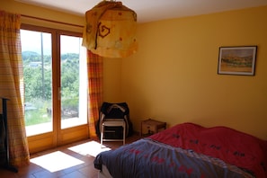 Relax in this serene bedroom with a large bed, chair, and small table, offering a peaceful retreat with a balcony overlooking lush greenery.