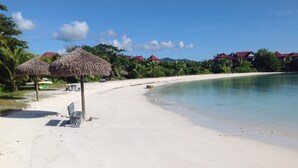 Uma praia com guarda-sóis de palha, um banco e vista clara para o oceano.