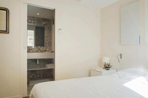 A hotel room with a bed, a nightstand with a lamp, a mirror, and a wardrobe with patterned tiles. - La Suite 35 (Nancy)
