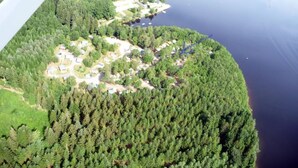 An aerial view of a lakeside community with dense forest, a small waterfall, and a cluster of houses. - Rental Neuvic Vallée Haute Dordogne (Neuvic)