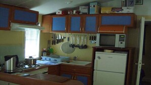 A compact kitchen with wooden cabinets, a microwave, a stove, and various utensils hanging on the wall. - Rental Neuvic Vallée Haute Dordogne (Neuvic)