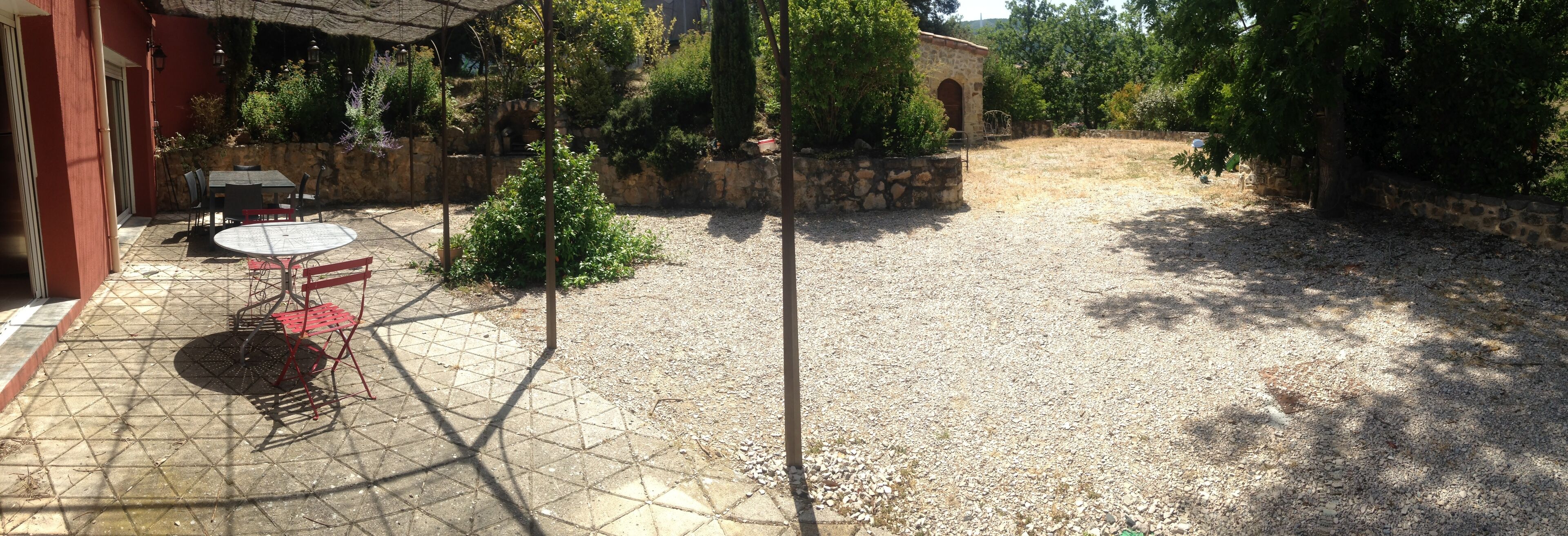 Un espace patio aménagé avec une table et des chaises, entouré de murs en pierre et de verdure.
