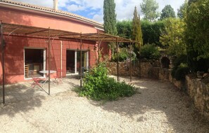 Une terrasse couverte avec une table et des chaises, un mur en pierre et un sol en gravier.