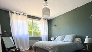 Un dormitori amb un llit, una finestra amb cortines, una làmpada i un mirall a la paret.