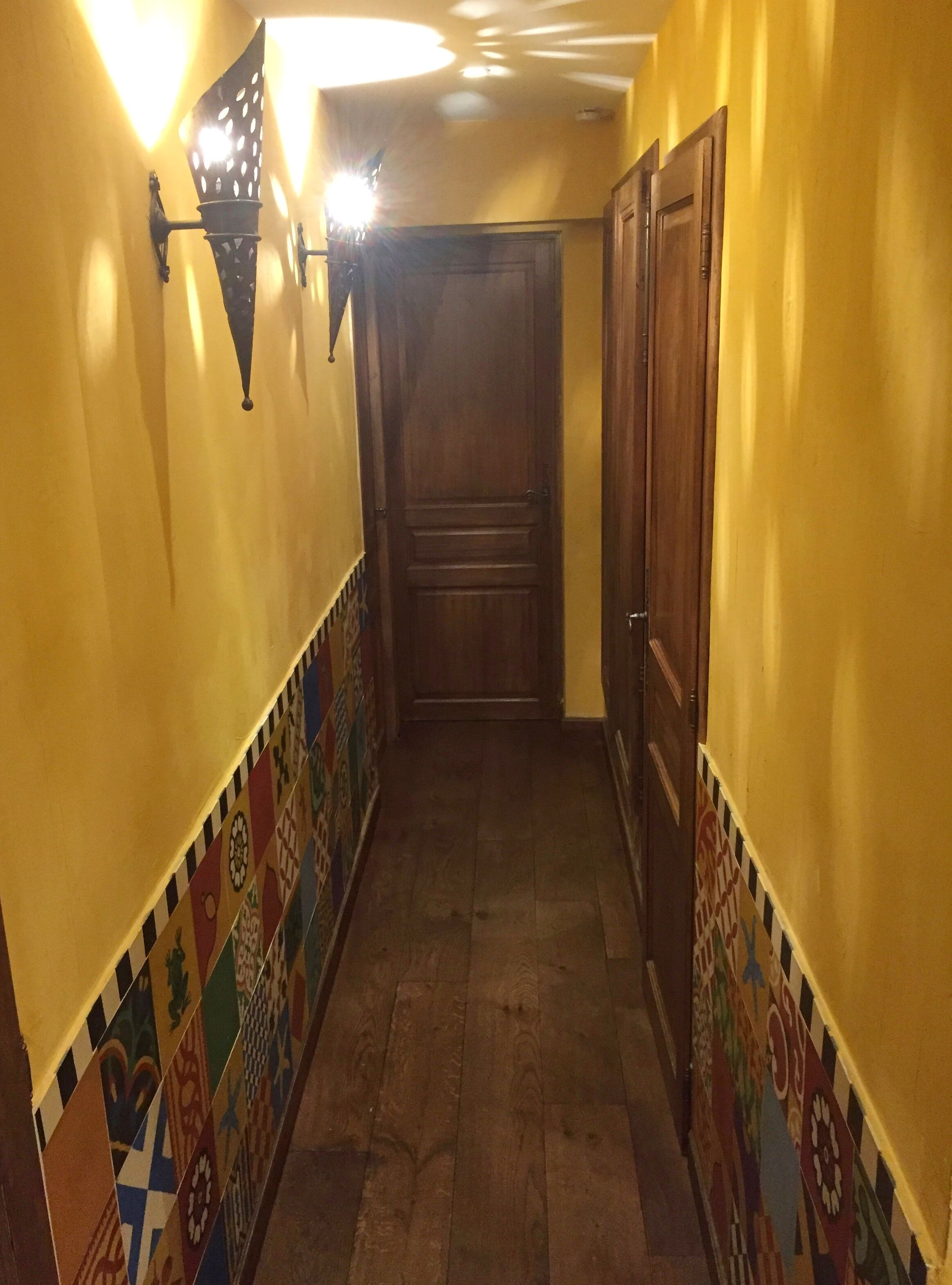Un pasillo con baldosas estampadas en las paredes, una puerta de madera al final y un accesorio de iluminación a la izquierda.