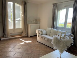 Et værelse med en hvid sofa, et lille hvidt skab og et vindue med gardiner.
