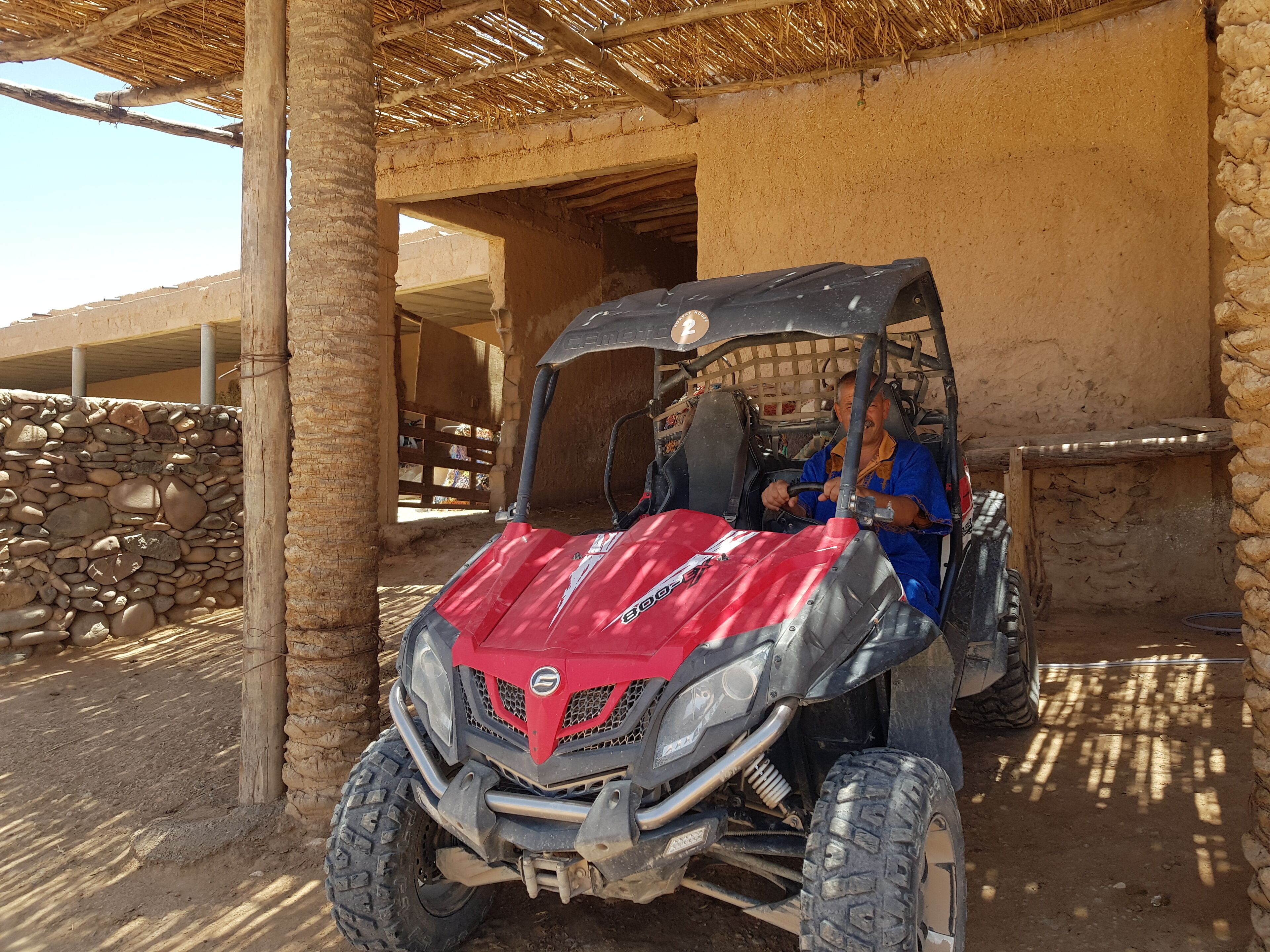 A red off-road vehicle parked under a thatched roof structure.