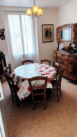 Ein Essbereich mit einem runden Tisch, Stühlen, einer Chandelier, einem Fenster mit Vorhängen, einem Holzschrank und einem gerahmten Bild an der Wand.