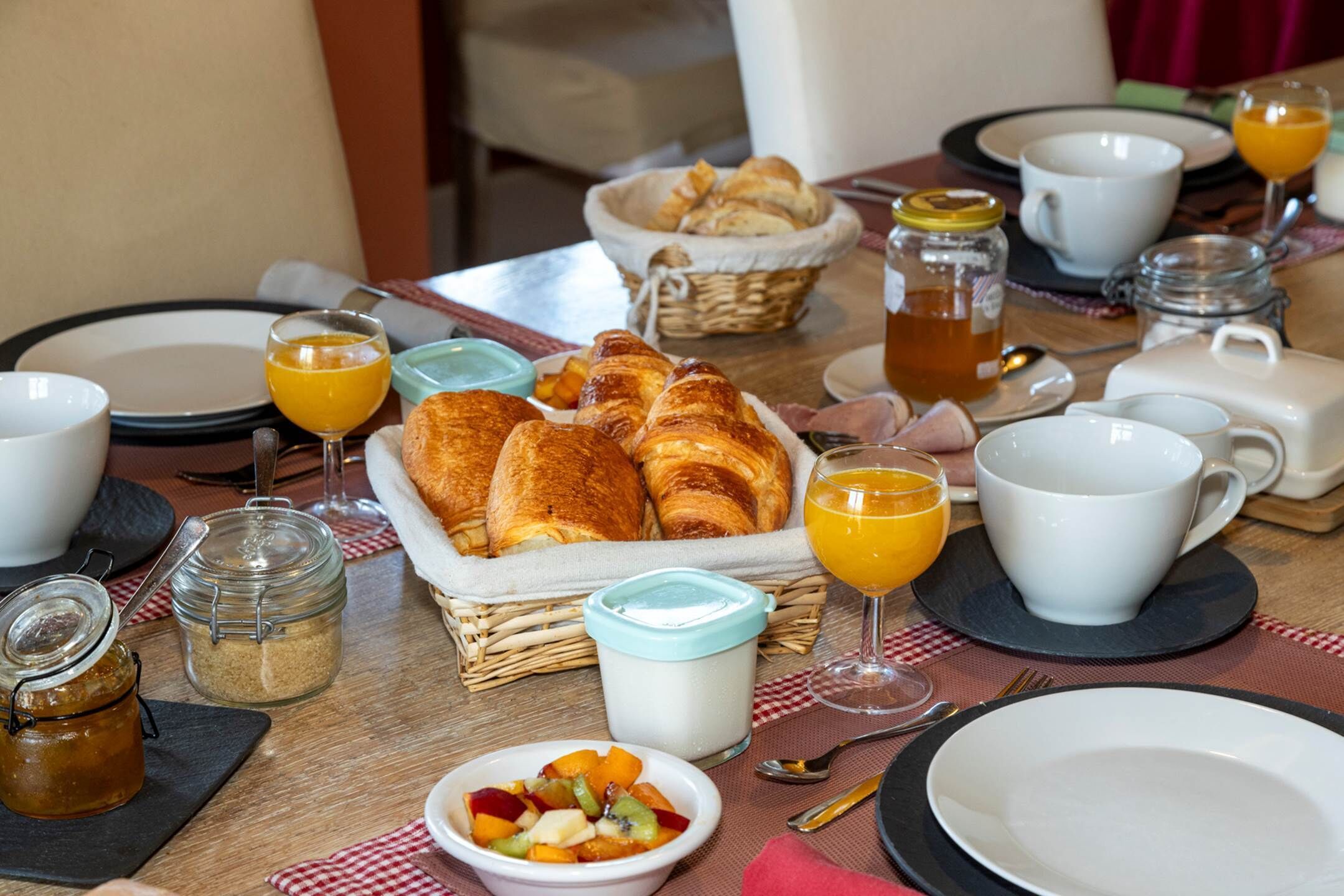A breakfast table set with croissants, orange juice, and a bowl of fruit salad.