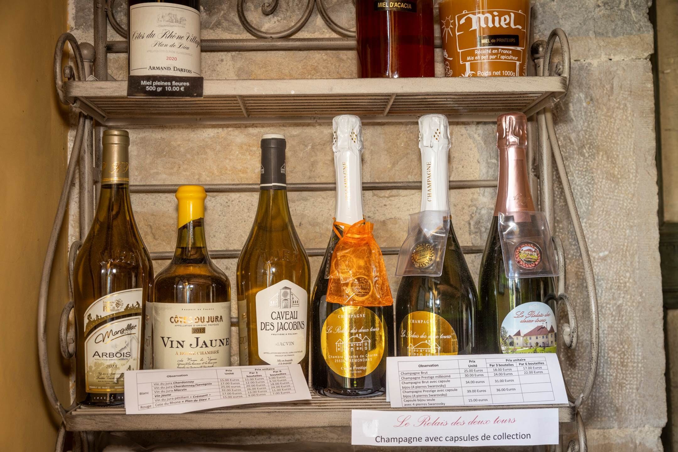 Una dispensa per vino con diverse bottiglie di vino e champagne, tra cui marchi come Arbois, Vin Jaune e Caveau des Jacobins.