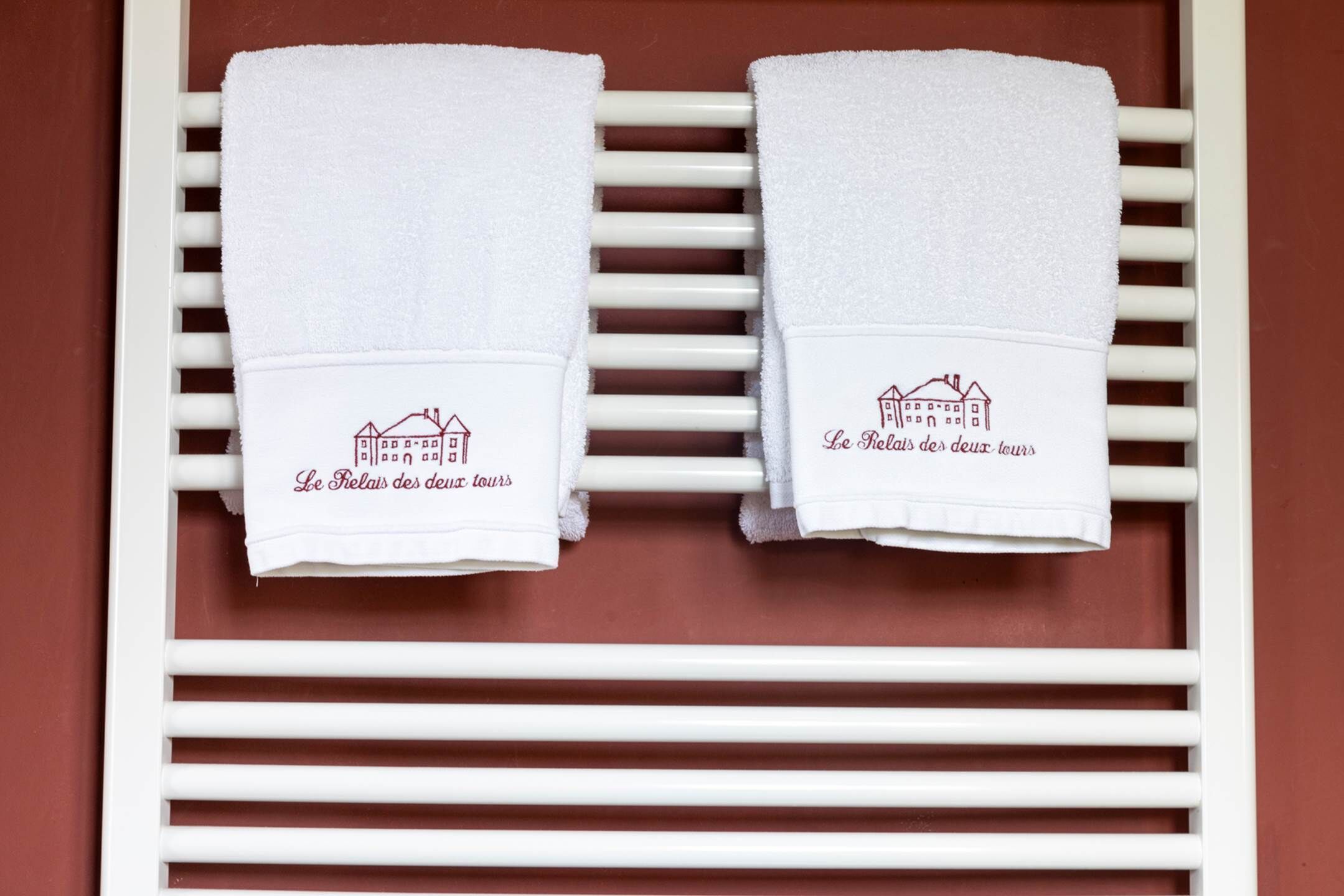 Two white towels with a building illustration and text on a white towel rack against a brown wall.