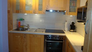 A kitchen with wooden cabinets, a stainless steel sink, a stove, and a microwave. - Apartment "Bellevue" Les Breuleux, Jura, Switzerland (Les Breuleux)