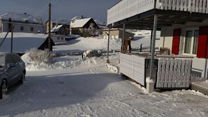 A snow-covered residential area with houses, a car, and a covered porch. - Apartment "Bellevue" Les Breuleux, Jura, Switzerland (Les Breuleux)