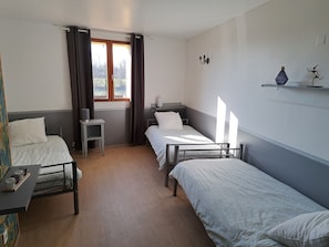 Quarto com duas camas de solteiro, uma mesinha, uma cadeira, uma janela com cortinas e um nicho na parede com objetos decorativos.