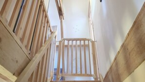 Un escalier en bois avec une rampe, menant à un palier éclairé par un luminaire au plafond.
