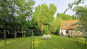 Une cour arrière verdoyante avec une table et des chaises en bois, un fil à linge et une maison avec un toit en tuiles.