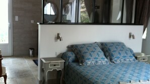 Une chambre à coucher avec un grand lit, une table de chevet, une commode, un miroir et une fenêtre avec des rideaux.