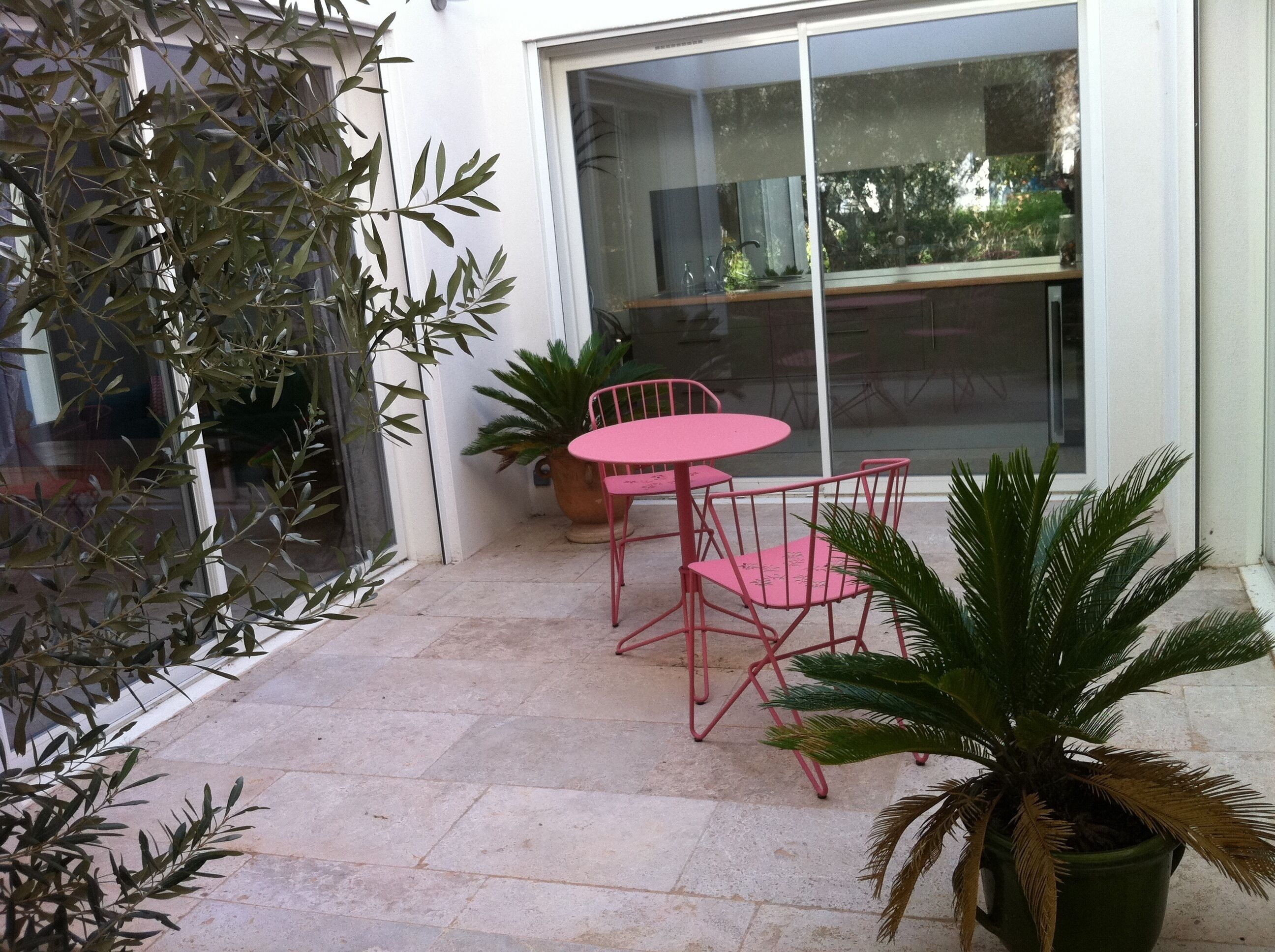 Un patio con mesa y sillas, plantas en macetas y un ventanal grande.