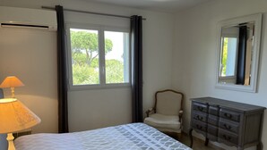 A bedroom with a bed, a dresser, a chair, a window with curtains, and a lamp.