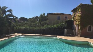 A clear swimming pool with a tiled edge, surrounded by a fence and greenery.