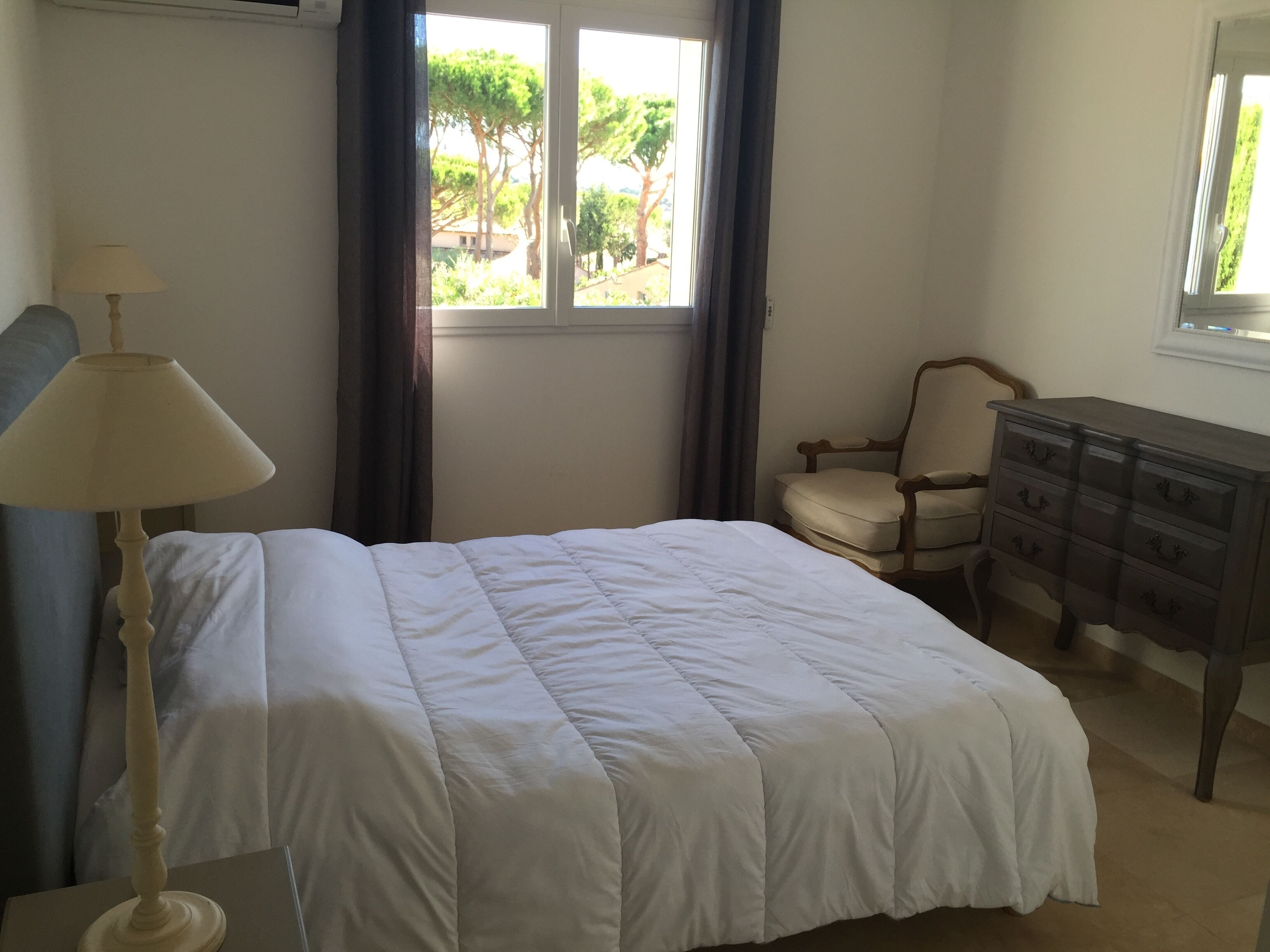 A bedroom with a bed, a dresser, a chair, and a window with curtains.