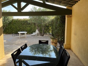 Eine Terrasse im Freien mit einem runden Glastisch und Stühlen, umgeben von Kies und einer Hecke.