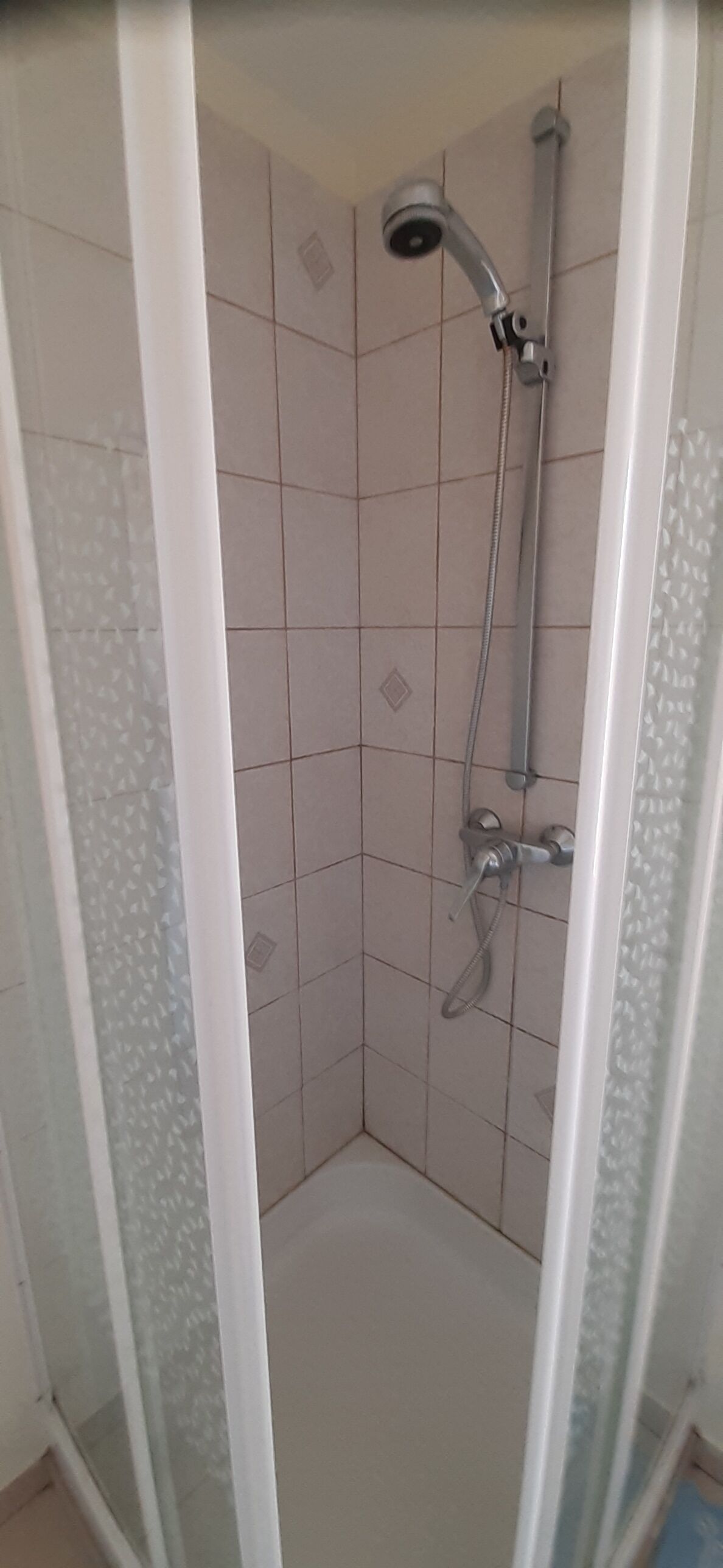 A glass-enclosed shower stall with a handheld showerhead and a wall-mounted faucet.