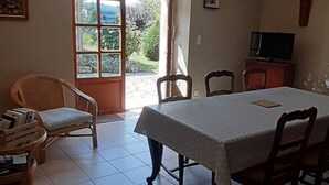 Un espace repas comprenant une table et des chaises, un téléviseur et une vue sur la verdure environnante.