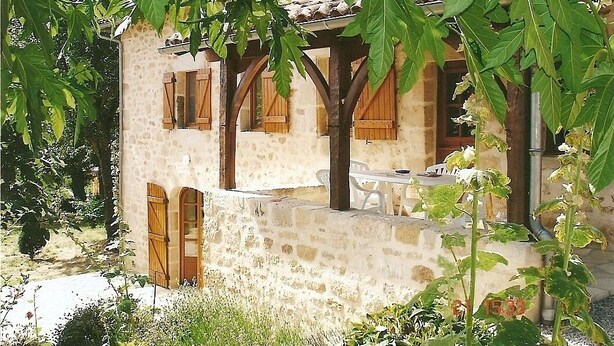 Un bâtiment en pierre avec des volets en bois, un balcon et une table à l’extérieur.