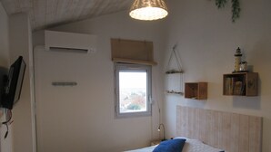 A bedroom with a bed, a window, a wall-mounted shelf with books, and a hanging light fixture.