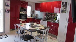 A modern kitchen with red cabinets, stainless steel appliances, and a dining area with a table and chairs.
