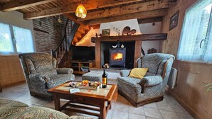 A cozy living room with a fireplace, two patterned armchairs, a coffee table with snacks, and a television. - Gîte rural des Gravets, shared pool (Sigalens)