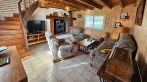 A cozy log cabin interior with a fireplace, wooden furniture, and a television. - Gîte rural des Gravets, shared pool (Sigalens)
