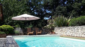 A swimming pool with a stone wall, wooden chairs, and an umbrella. - Gîte rural des Gravets, shared pool (Sigalens)