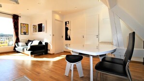 A modern living room with a sofa, a dining table, and a chair. There is a window with curtains, a painting on the wall, and a door. - COUP DE ❤️ LA MOUETTE DEAUVILLAISE🐦classified 4☆ Tennis-Pool-Parking-Linen-Wifi (DEAUVILLE)
