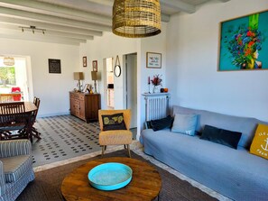 A cozy living room with a sofa, a patterned rug, a wooden coffee table, and a dining area with a wooden table and chairs.